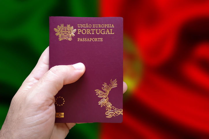 Man's hand holding Portuguese passport with defocused Portuguese flag in the background