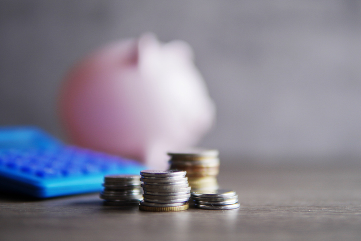 An out of focus piggy bank, with coins stacked in the foreground